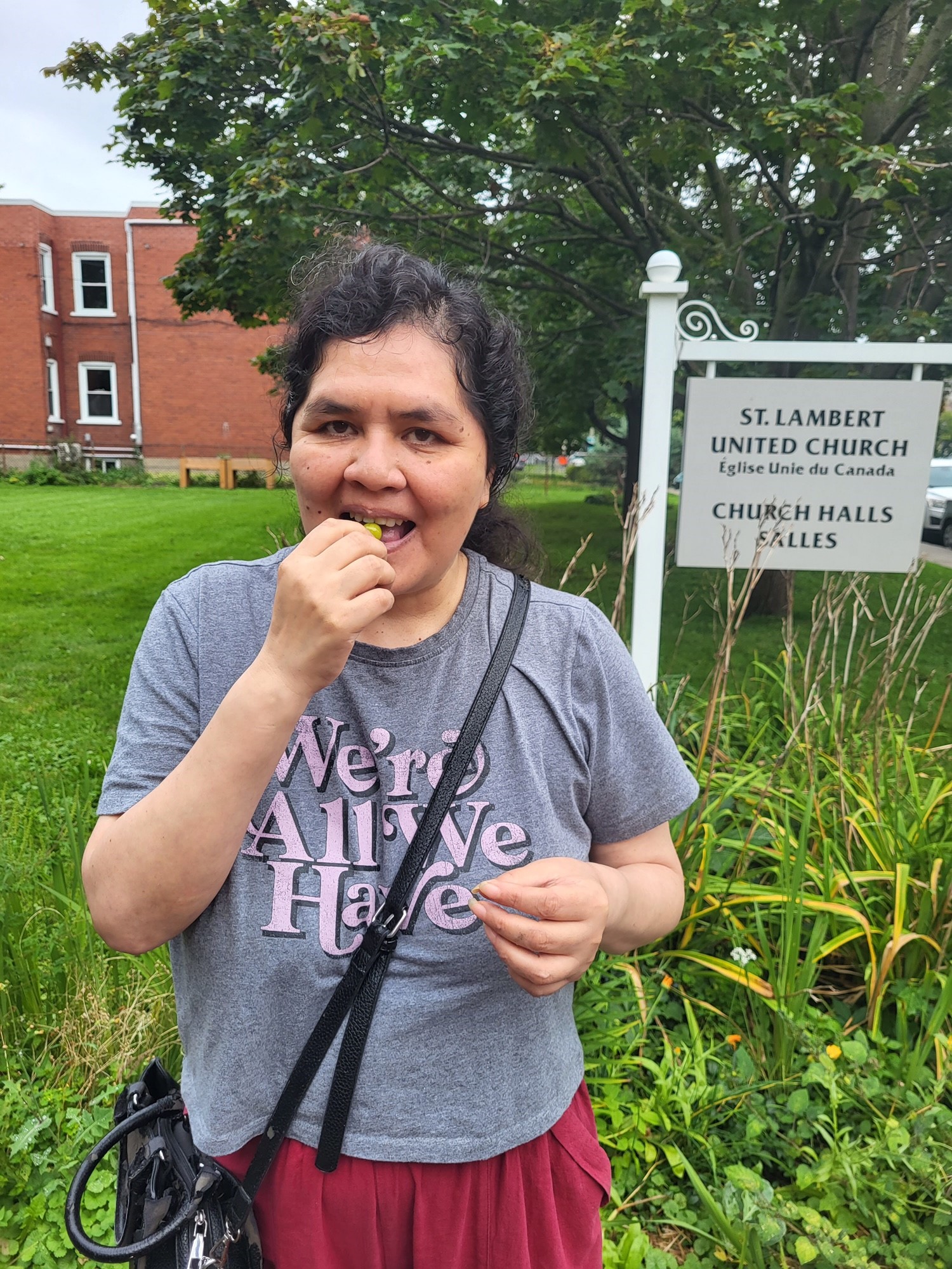 une femme mangeant une cerise de terre devant l'enseigne de l'Église Unie Saint-Lambert