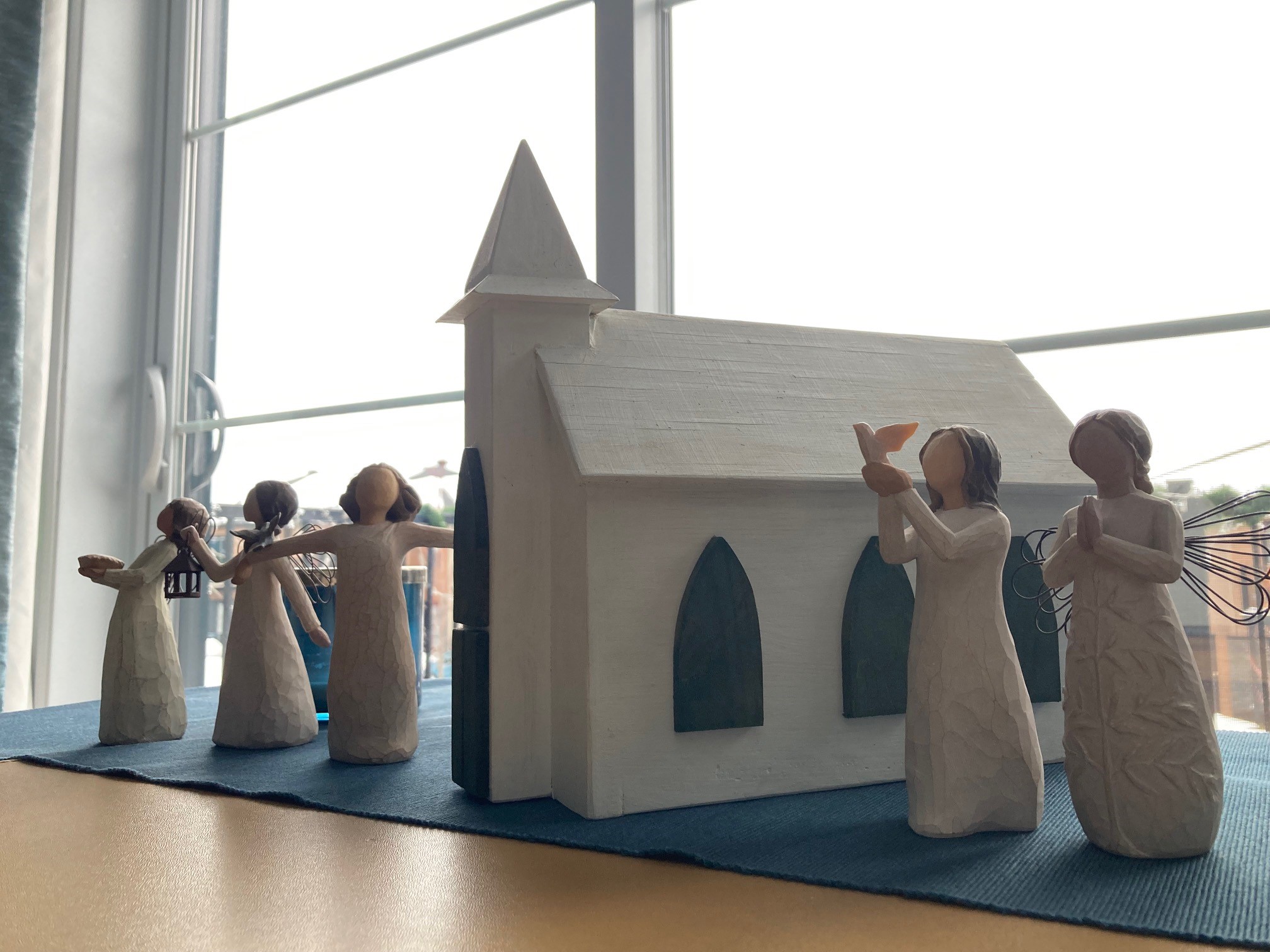 Wooden model of church in front of windows, surrounded by angel figurines